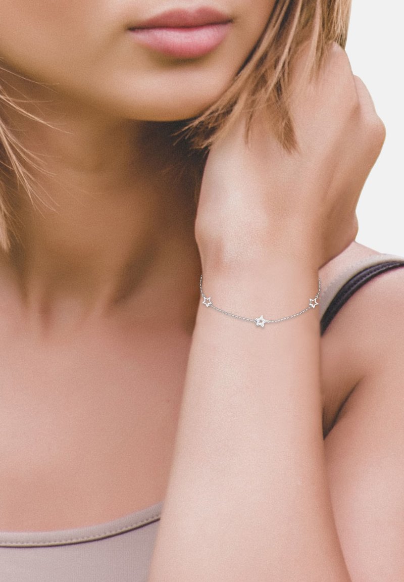 Bracciale d'argento con pendenti a forma di stella, catena leggera e finitura lucida, indossato su un polso con tonalità di pelle morbide.