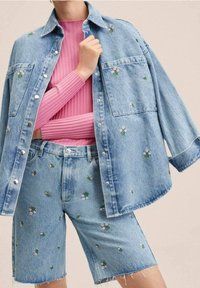 Zestaw z jasnoniebieską kurtką dżinsową i szortami, z kwiatowym haftem. Kurtka ma zatrzaski i dwie przednie kieszenie. Pod spód założona różowa bluzka z prążkowanego materiału.