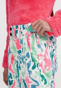 Pantalones coloridos y con estampado presentan una base blanca con formas abstractas en rosa, verde y azul. Tienen un botón y un cierre de gancho en la cintura.