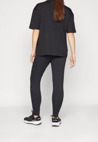 Černé nadměrné tričko a přiléhavé legíny, oboje z hladké látky. Černé sportovní boty s bílou podešví, pohled zezadu.