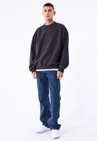 Sudadera gris con cuello redondo, con un sutil logotipo, combinada con jeans de mezclilla azul y zapatillas blancas sobre un fondo liso.