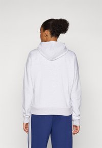 Sweatshirt cinza com capuz, de ajuste relaxado, com punhos e barra canelados. Apresenta uma textura suave e bolso canguru, combinado com calças de moletom azuis.