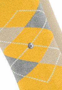 Gelbe, graue und beigefarbene Socken im Argyle-Muster mit strukturiertem Strick und einem kleinen silbernen Logodetail an der Seite.