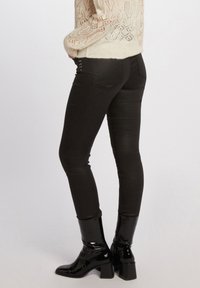 Jeans skinny neri con una tessitura liscia, dotati di borchie laterali e una vestibilità sartoriale, abbinati a stivali neri lucidi con tacco.