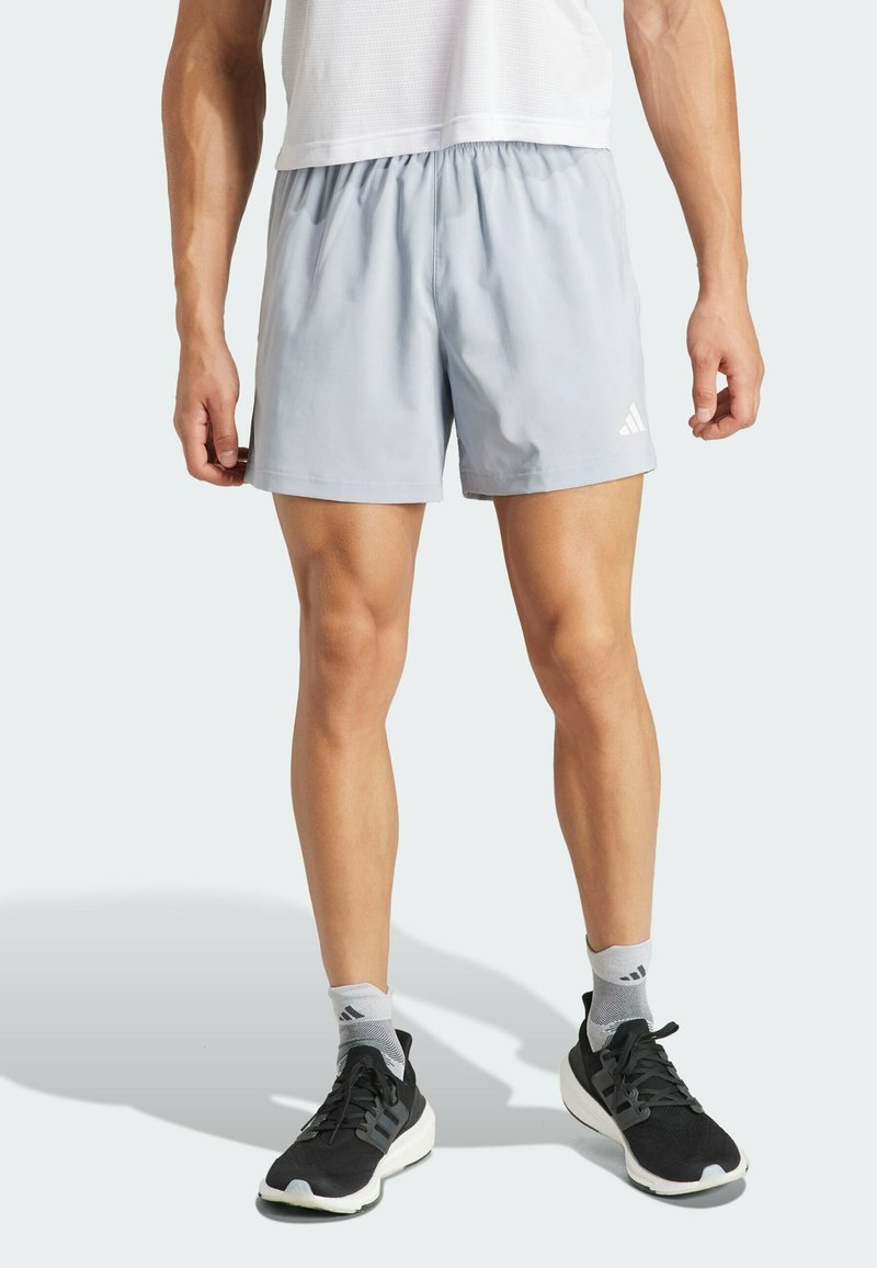 Pantalones cortos deportivos de color gris claro con una cintura elástica y un logo de Adidas en el dobladillo inferior. Se llevan con zapatillas negras y calcetines grises.