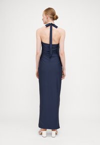 Marinblå halterneck-kjole med et tætsiddende bodice og rynket tekstur, der har en rygsnørredetalje og en gulvlængde silhuet.