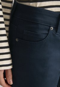 Marineblauwe broek met een zijzak, een gladde textuur en stikseldetails, gecombineerd met een beige en zwart gestreept overhemd met lange mouwen.