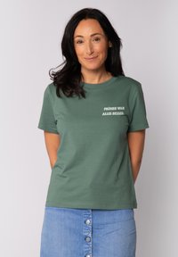 Grünes Baumwoll-T-Shirt mit kurzen Ärmeln und Rundhalsausschnitt; auf der Vorderseite mit weißem Text "FRÜHER WAR ALLES BESSER".