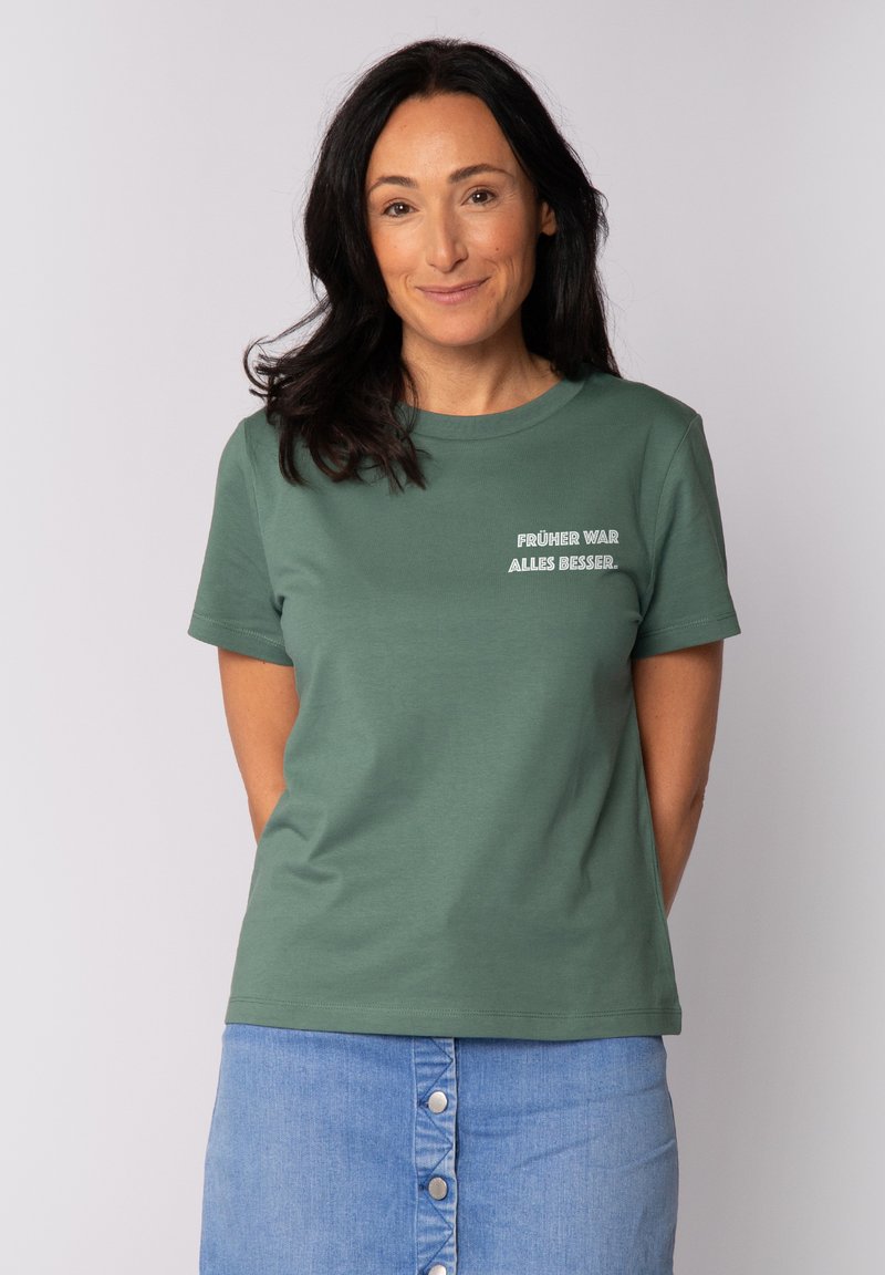 Grünes Baumwoll-T-Shirt mit kurzen Ärmeln und Rundhalsausschnitt; auf der Vorderseite mit weißem Text "FRÜHER WAR ALLES BESSER".