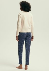 Kremowa bluzka z długim rękawem i okrągłym dekoltem, w zestawie z granatowymi spodniami piżamowymi w beżowy kwiatowy wzór. Miękka tkanina, luźny krój.