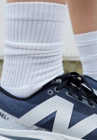 White ribbed socks worn with blue and gray athletic shoes featuring a prominent white logo, textured patterns, and black laces.