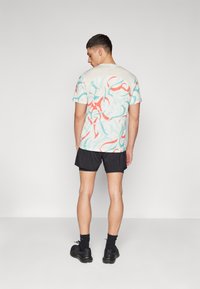 Short-sleeve t-shirt with a colorful abstract design in red, blue, and cream. Paired with black shorts and black sneakers.