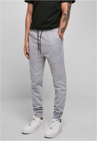 Pantalons de survêtement gris en matériau doux, avec poches latérales, taille élastique avec cordon de serrage et jambes fuselées. Associés à des baskets blanches.