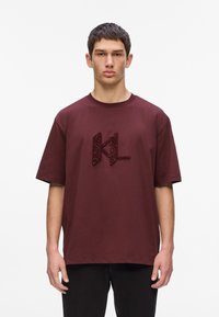 Burgundijas krāsas kokvilnas T-krekls ar īsām piedurknēm, ar teksturētu tumši sarkanu "KL" logotipu priekšpusē. Vienkāršs, relaksējošs griezums.