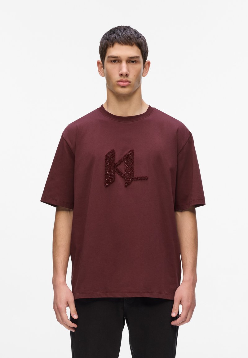 Burgundijas krāsas kokvilnas T-krekls ar īsām piedurknēm, ar teksturētu tumši sarkanu "KL" logotipu priekšpusē. Vienkāršs, relaksējošs griezums.