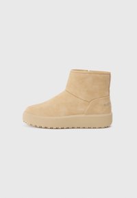 Bottines beige en daim doux avec une finition texturée, arborant un design minimaliste et une semelle en caoutchouc épaisse pour l'adhérence.