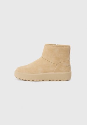 Bottines beige en daim doux avec une finition texturée, arborant un design minimaliste et une semelle en caoutchouc épaisse pour l'adhérence.