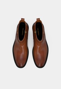 Brown leather ankle boots with a rounded toe, zipper closure on side, and contrasting black sole. Smooth texture and minimal design.