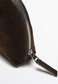 Borsa in suede marrone con una cerniera metallica e un'impugnatura in pelle. La forma è arrotondata con una finitura liscia e testurizzata.