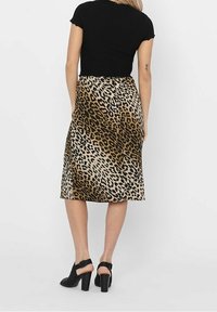Dyrprint nederdel med et beige og brunt leopardmønster, mellemlang, glat tekstur. Båret med en tætsiddende sort top og sorte sko med blokhæl.