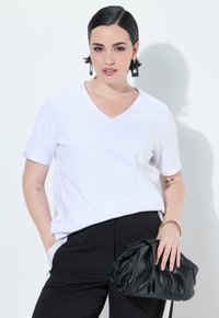 T-shirt bianco a maniche corte con scollo a V, vestibilità rilassata, abbinato a pantaloni neri e una grande borsa nera arricciata. Tessuto di superficie liscia.