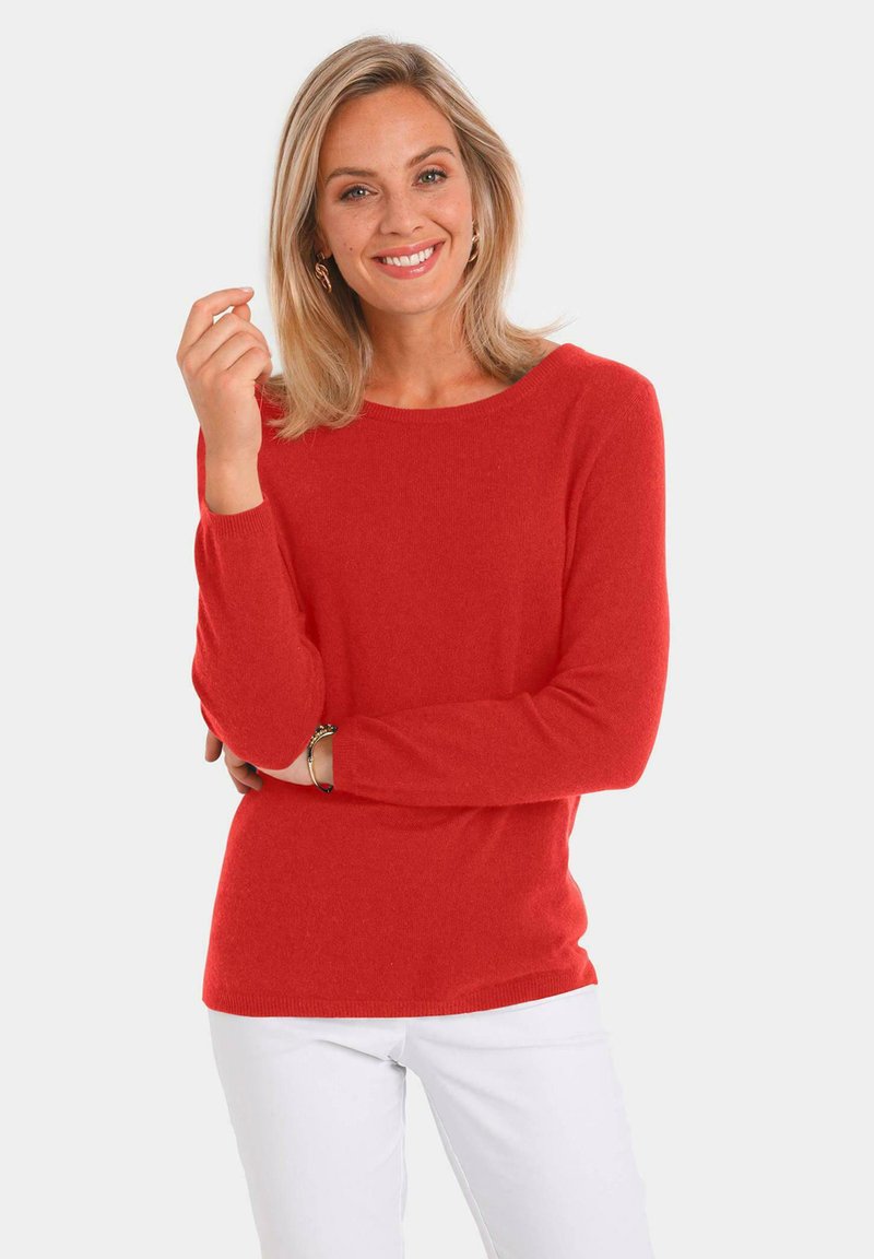 Roter Pullover mit langen Ärmeln und rundem Halsausschnitt, weicher Struktur und gerippten Bündchen, kombiniert mit weißen Hosen. Schlichtes und modernes Design.