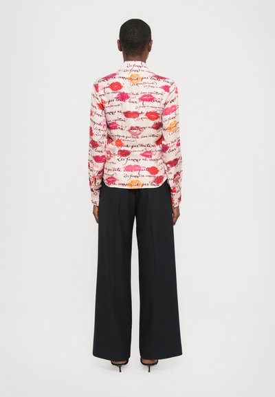 Long-sleeve, collared shirt in white with red, pink, and orange lip prints and handwritten text; worn with black wide-leg pants.