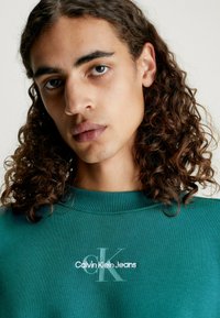 Sudadera verde con scollo a coste, caratterizzata da logo ricamato "Calvin Klein Jeans" e un sottile elemento di design CK. Tessuto testurizzato.