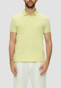 Helles gelbes Polo-Shirt aus Baumwolle mit klassischem Kragen und kurzen Ärmeln, versehen mit einem dezenten Logo auf der linken Brust.