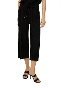 Zwarte geplooide culottes van lichtgewicht stof met een elastische tailleband en trekkoord. Gecombineerd met zwarte sandalen met hoge hakken en banden.