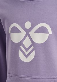 Motif abstrait d'abeille blanche avec des formes géométriques sur le devant d'un tissu lavande, probablement un sweat-shirt ou un hoodie.