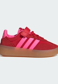 Röda och rosa sneakers med en överdel av mocka, tre kontrasterande ränder, ett kardborreband och en genomskinlig sula. Rundad tådesign.