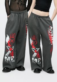 Graue weite Jogginghose mit roten und weißen Grafikdrucken, darunter Hasen- und Engelsmotive; elastischer Bund und Seitentaschen.