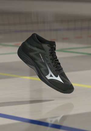 Sort sportssko med sølvlogo og "Lightning Select" tekst, svævende over en lyst farvet sportsbane med farvede linjer.