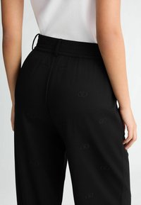 Pantaloni neri con vita elasticizzata, caratterizzati da un motivo con logo ricamato. Texture liscia e vestibilità comoda, progettati per il massimo comfort.