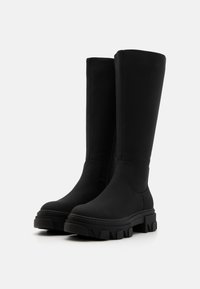 Botas negras hasta la rodilla hechas de un material suave con suela gruesa, punta redonda y un detalle de costura mínimo. Sin hardware visible.