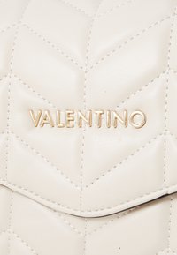 Quiltana bež usnjena torba z zlatim logotipom "VALENTINO" z diskretnim šivi in zaobljenim zapiranjem na pokrovčku.