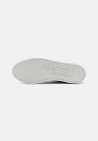 Suela de zapato de goma blanca con agarre texturizado, que presenta el nombre de la marca grabado "SELECTED / HOMME" y la talla "42" en la superficie.