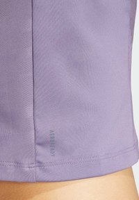 Top atlético de color lila hecho de un tejido suave y stretch, con costuras laterales y una etiqueta de marca sutil cerca del dobladillo.