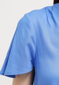 Top blu corto a maniche corte realizzato in tessuto morbido. Presenta una vestibilità morbida con una sottile texture e un orlo leggermente curvo alle maniche.