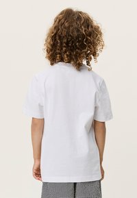 Λευκό βαμβακερό T-shirt με κοντά μανίκια, με άνετη εφαρμογή και στρογγυλή λαιμόκοψη. Ορατή ραφή στην πλάτη, σε συνδυασμό με ριγέ παντελόνια.