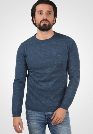 Marineblauer langärmeliger Strickpullover mit Rundhalsausschnitt und strukturiertem Stoff. Kombiniert mit hellblauen, abgewetzten Jeans.