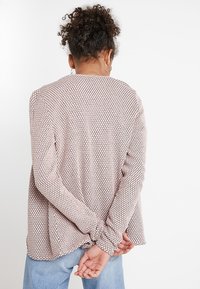 Růžová košile s dlouhým rukávem a šestibokým vzorem, volného střihu s manžetami na rukávech, doplněná modrými džínami.