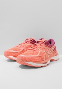 Scarpe da corsa leggere con tomaia in rete traspirante color corallo e viola, caratterizzate da una suola ammortizzata, un design con lacci e dettagli testurizzati.