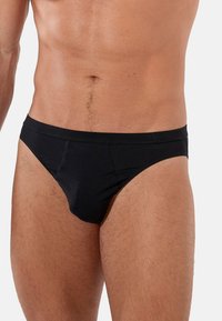 Schwarze Unterwäsche aus weichem Stoff, mit einem glatten Bund und einer konturierten Fronttasche für zusätzlichen Komfort. Minimale Nähte.