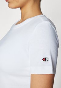 Hvit bomulls t-skjorte med korte ermer, med rund halsutskjæring og en liten brodert logo på venstre erme.