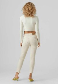 Bílý žebrovaný crop top spárovaný se světle béžovými slim-fit džíny, které mají hladký povrch a hnědou nášivku na zadní kapse. Zelené sandály na podpatku.