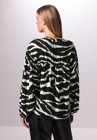 Langärmlige Bluse in Schwarz-Weiß mit Muster, locker geschnitten, mit einer gerafften Rückennaht und weichem Stofftexture.