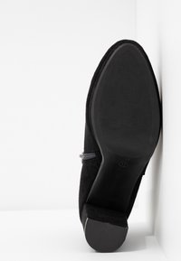 Chaussure en daim noir avec petit talon bloc vue du côté de la semelle, sur fond blanc en coin, taille 37 marquée sur la semelle.