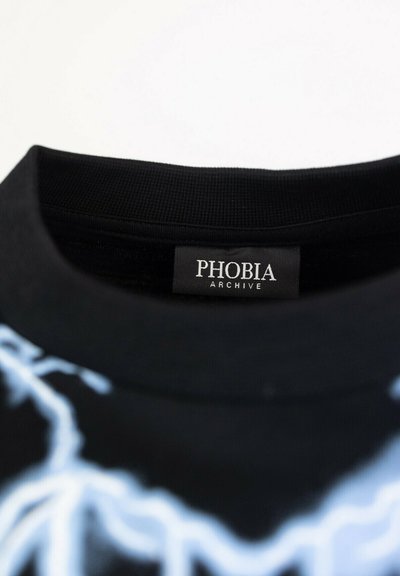 T-shirt nera con colletto a costine, caratterizzata da grafiche di fulmini blu e un'etichetta "PHOBIA ARCHIVE" cucita all'interno del collo.